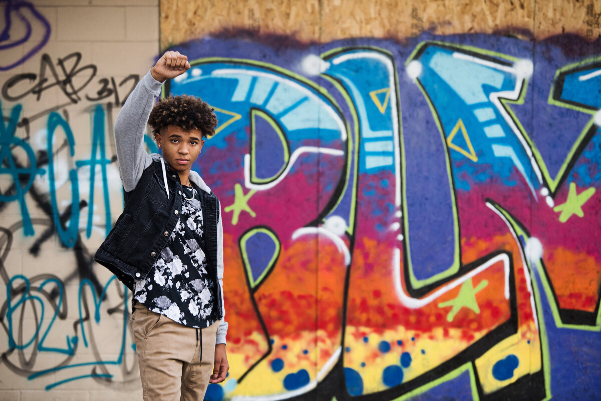 senior photo of boy with fist raised and black lives matter mural in urban minneapolis