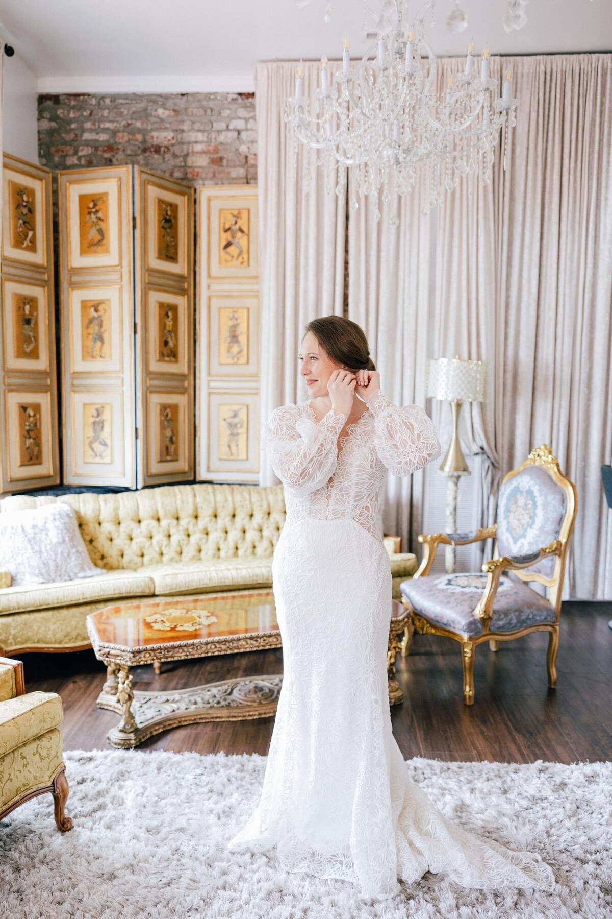 A woman in an elegant white lace dress standing in a luxurious room with vintage furniture and decor.