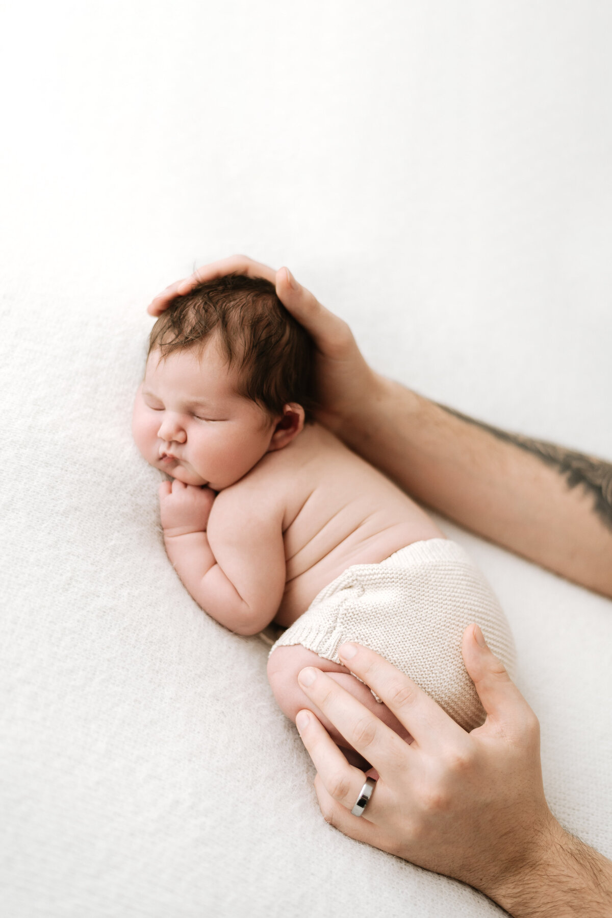 Baby girl sleeping on a white blanket with dad holding her head at a newborn  photography photoshoot in Billingshurst