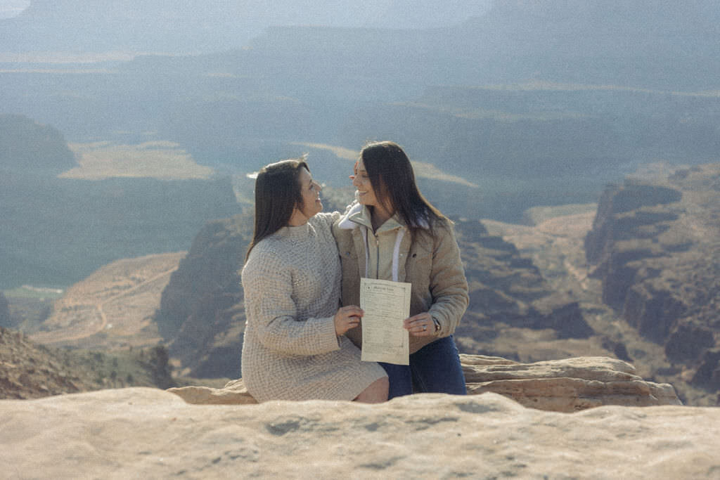 A couple sitting on a rock showing off a marriage certificate.