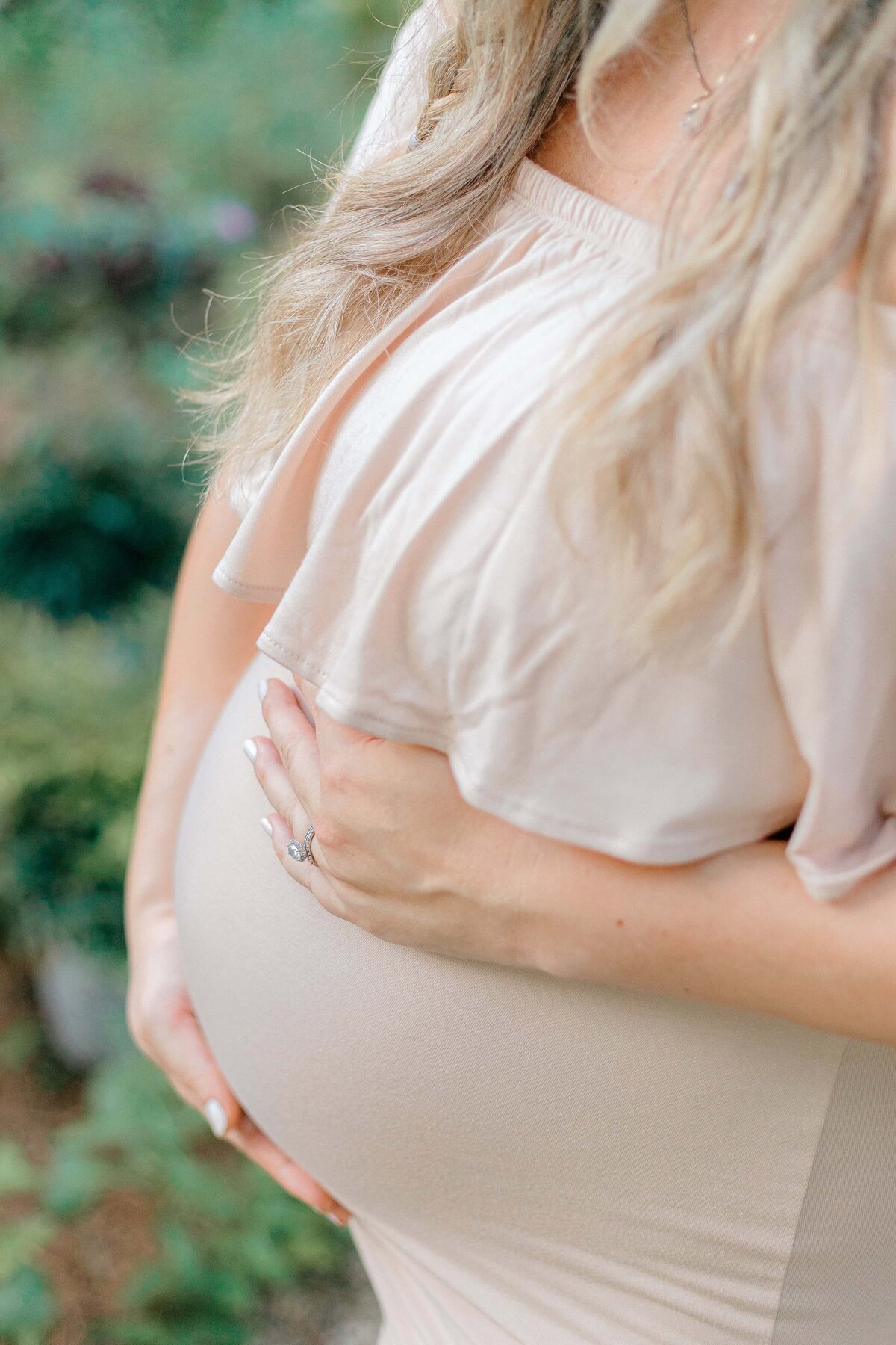 A pregnant woman is wearing a light pink dress and embracing her belly with Hilton Head Maternity Photographer, Lamp and Light Photography.