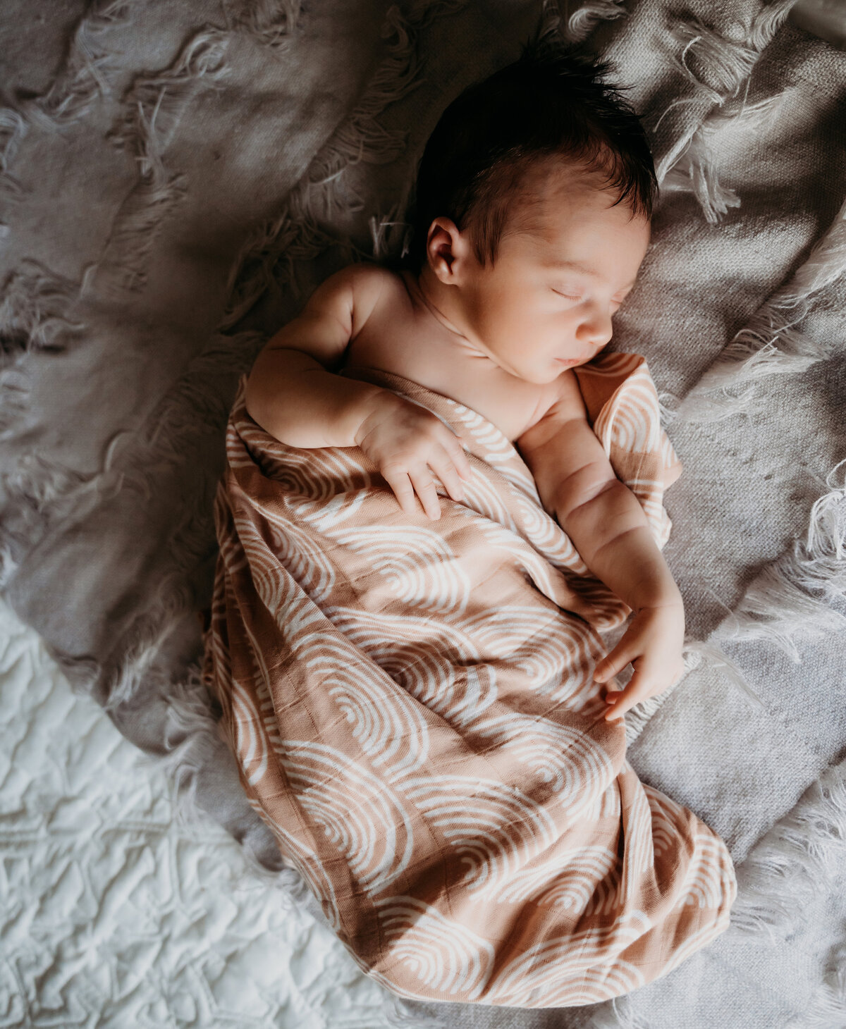 Newborn Photographer, a baby sleeps cozily wrapped in blankets on the bed covers