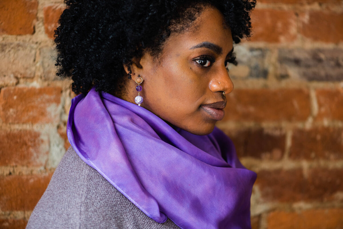 A stunning profile of a black woman wearing a purple scarf and earrings by Denise Van, a Northern VA brand photographer