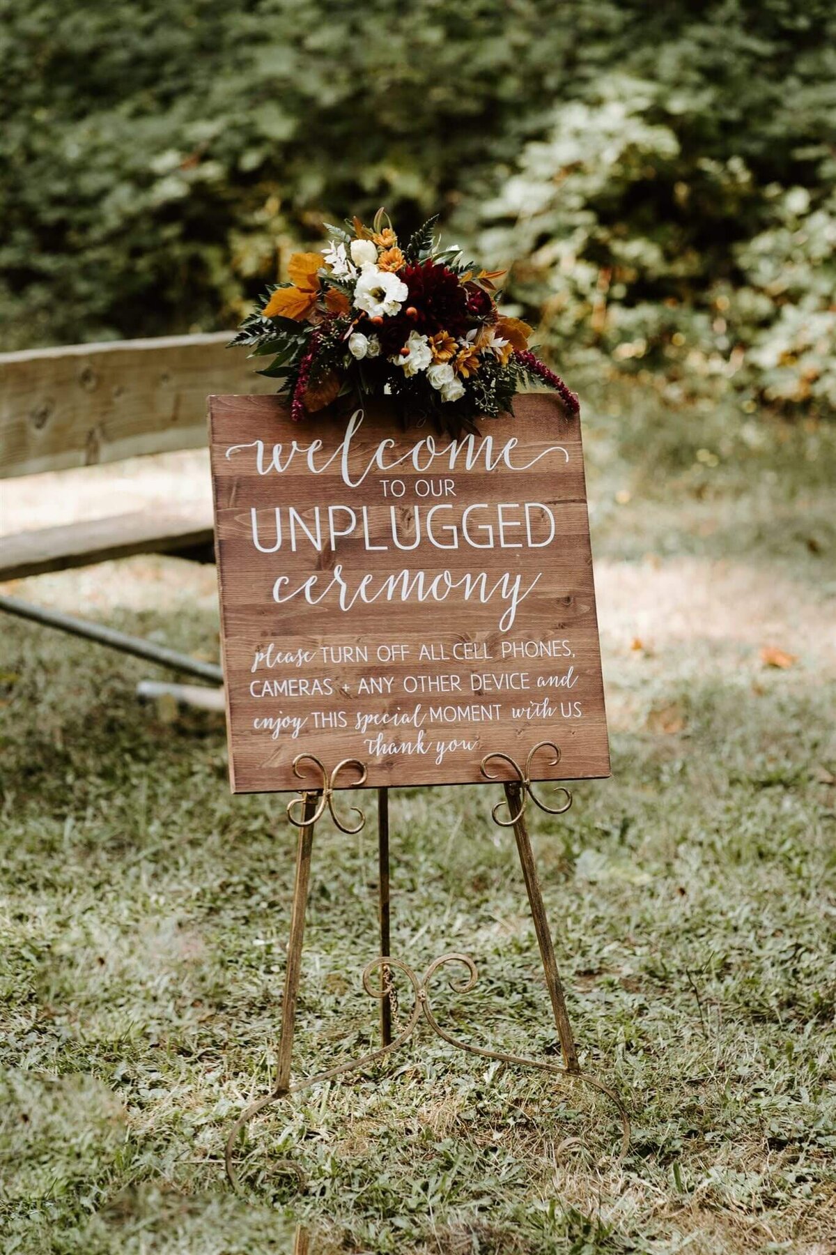 Unplugged ceremony sign with fall floral arrangement atop it.
