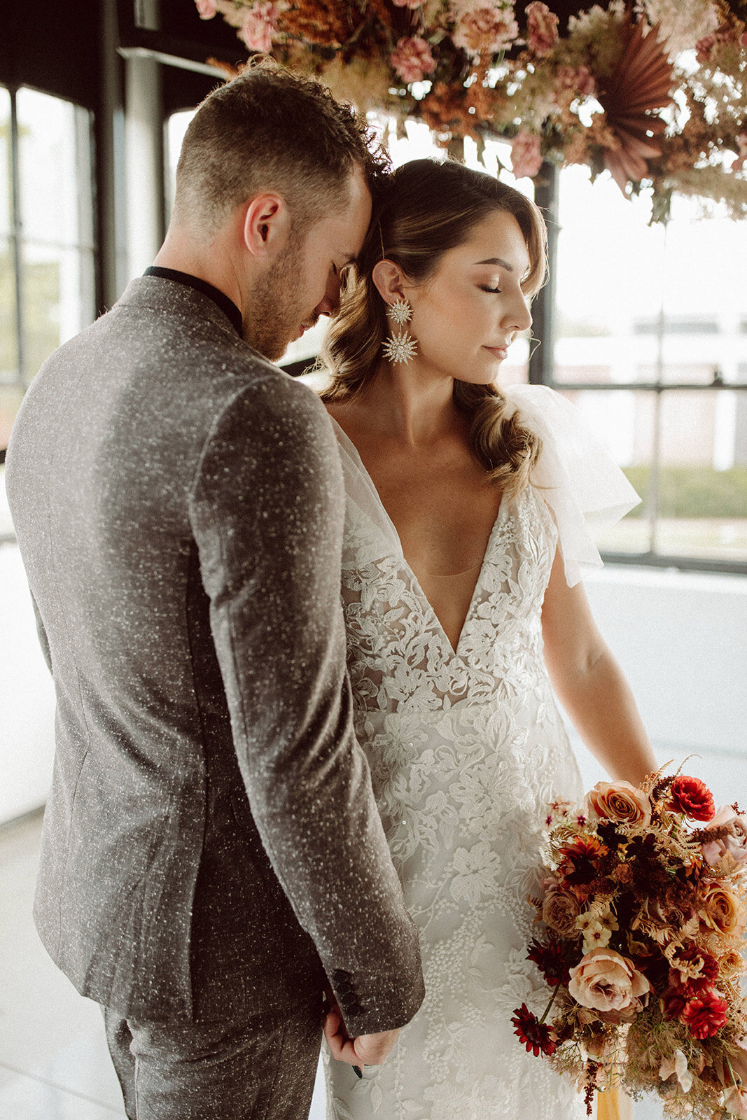 Groom wearing a gray suit leans into a bride wearing a white wedding gown while holding a bouquet.