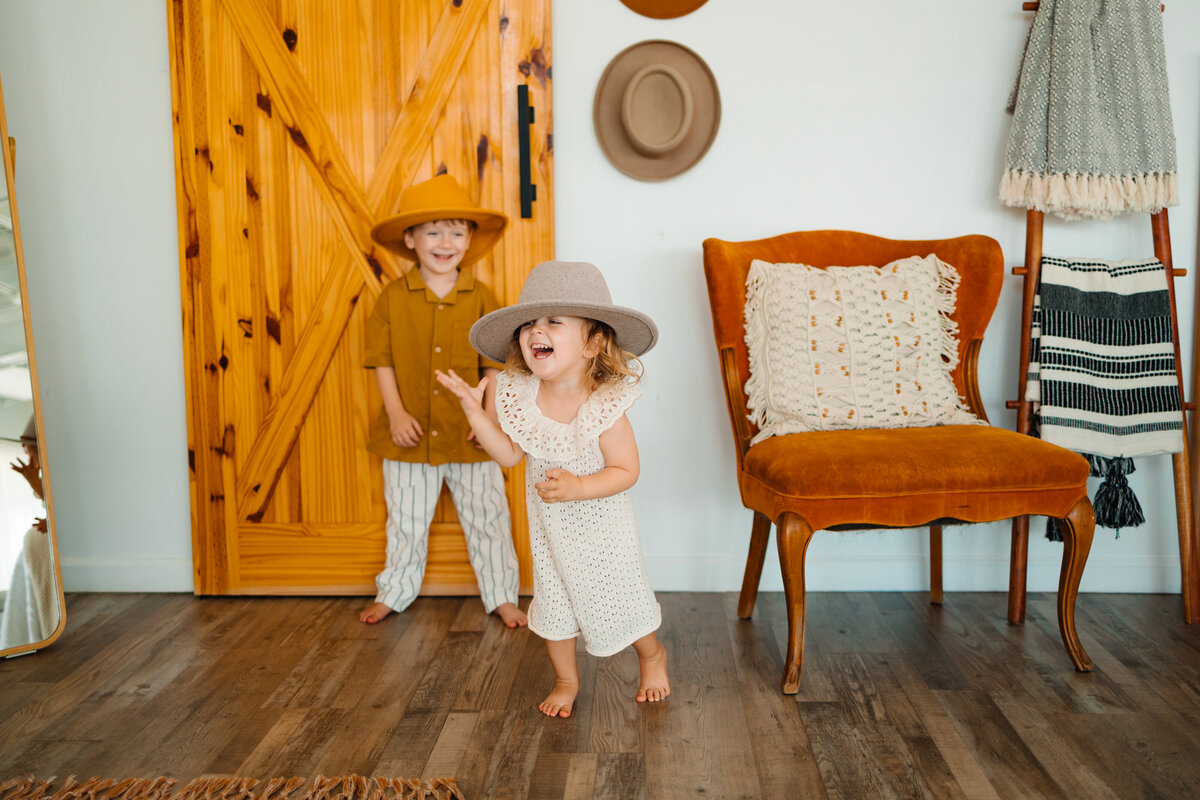 the warmth of Albuquerque portrait photography with this charming image of a family outside a cabin. The woman holds a baby girl wearing an orange cap with her eyes closed, while the man looks at them with the child on his shoulders.