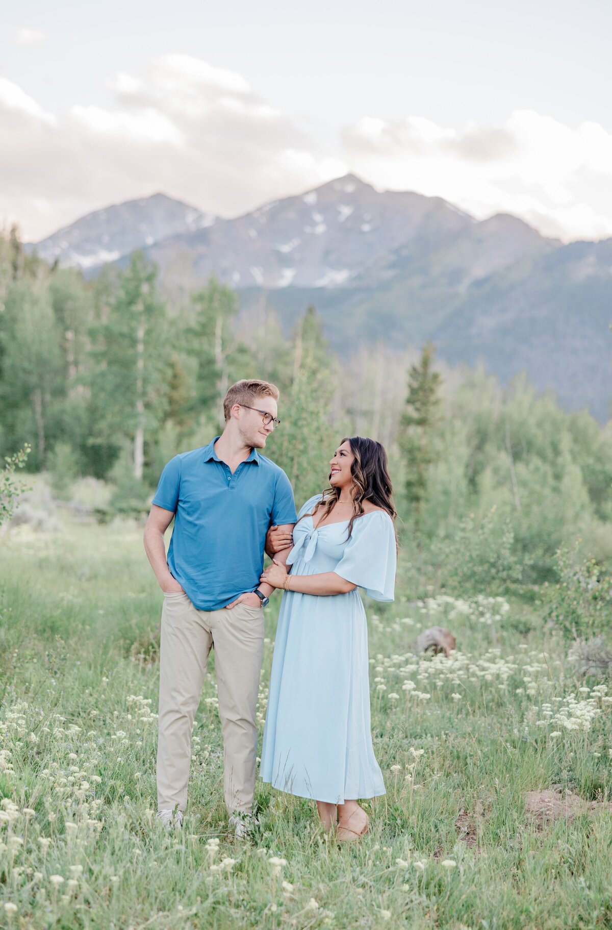 A woman in a blue dress laughs with her husband while exploring a mountain wildflower field