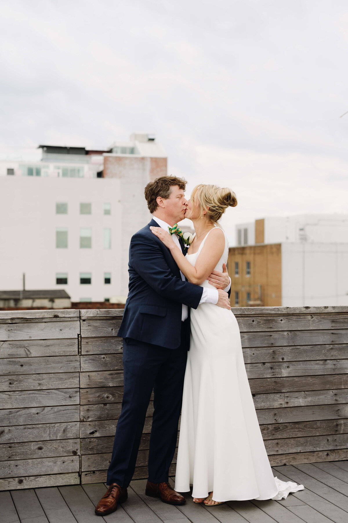 outdoor wedding photo with man and woman hugging as they kiss on a roof top in Richmond on a cloudy day