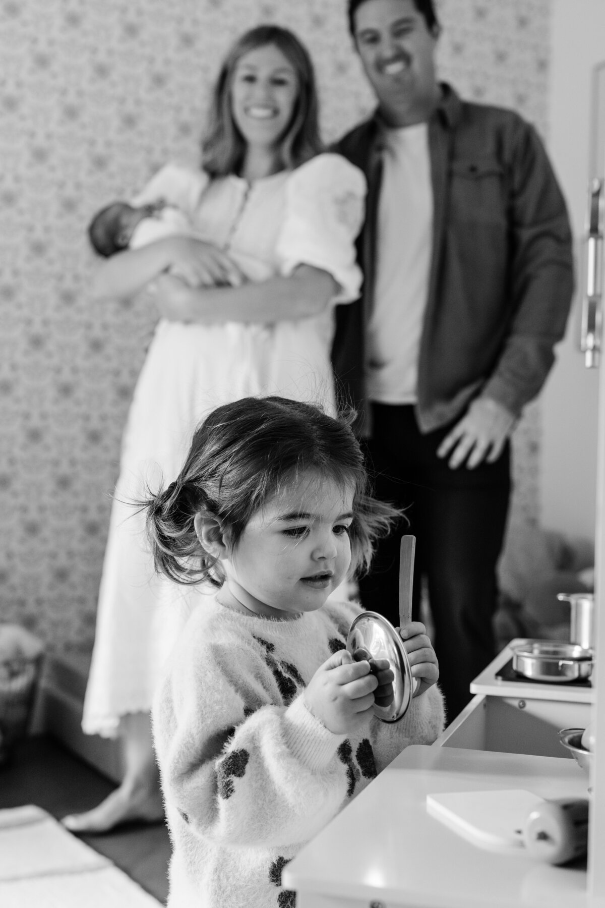 girl-playing-with-toy-kitchen-and-parents-in-the-background