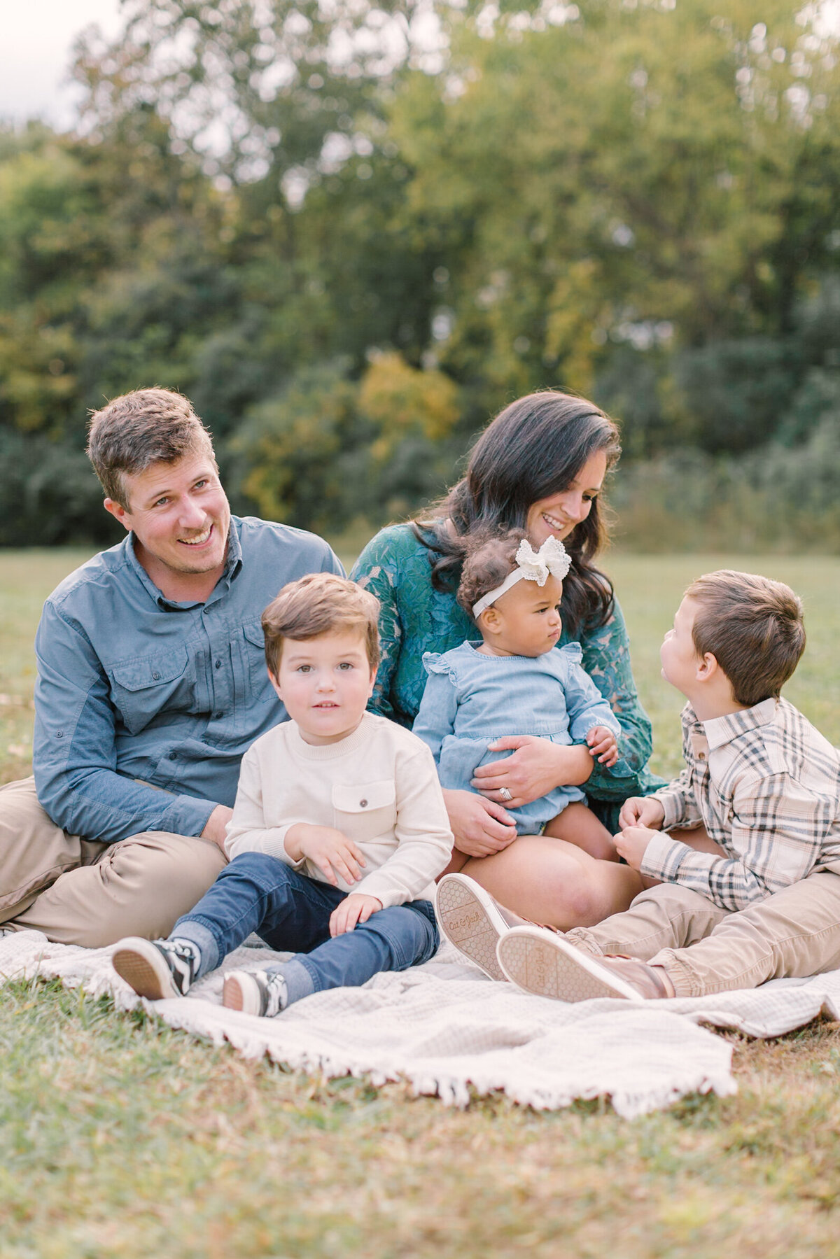 A family of five sitting on a blanket together in a grassy field at sunset — Raleigh portrait photography.