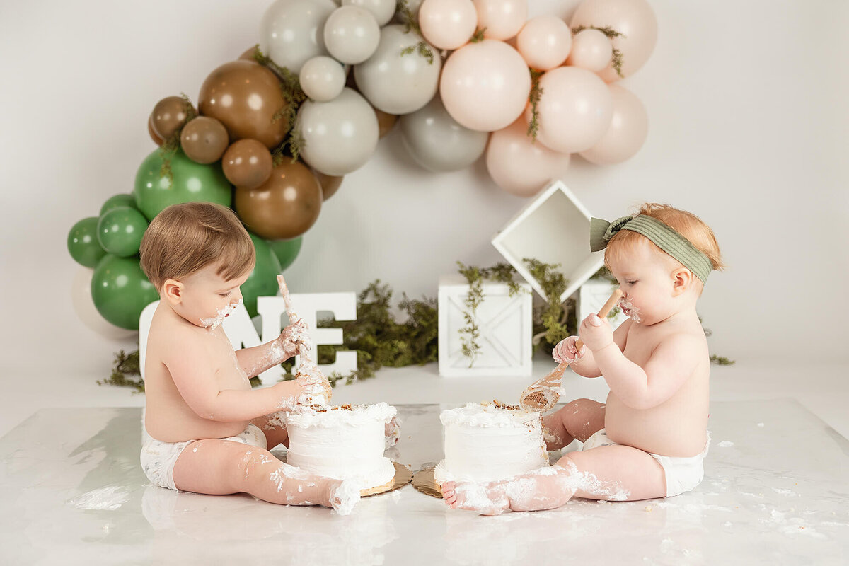 A twin brother and sister share cake during their birthday cake smash session.