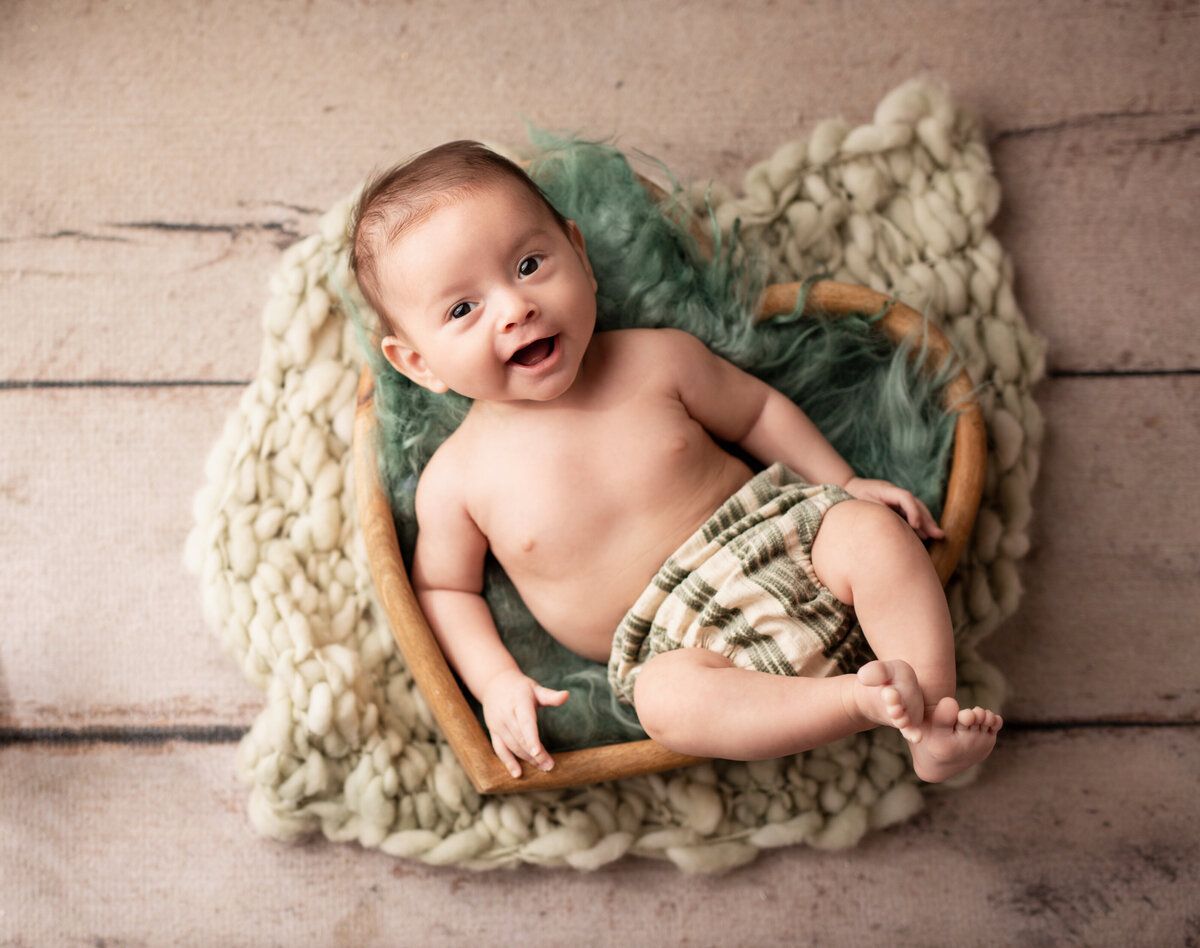 baby in heart basket with green blanket smiling looking at camera