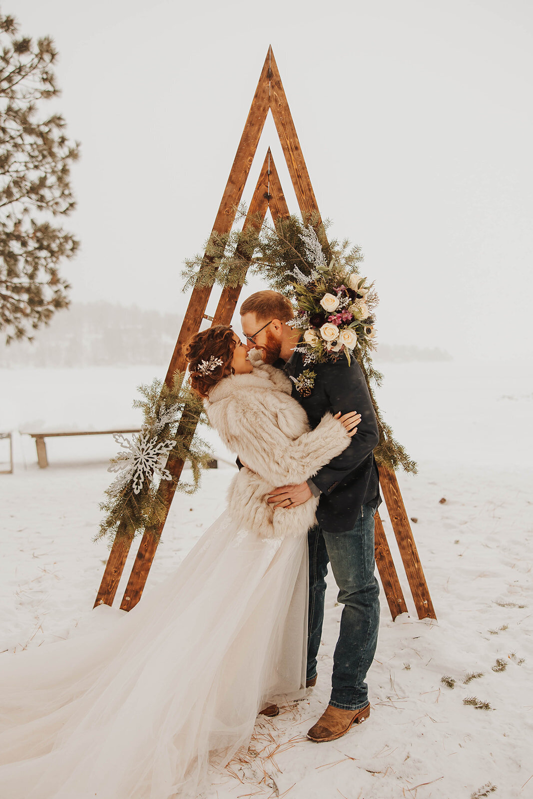 Bride and groom kissing at an altar in the snow during a winter wedding.