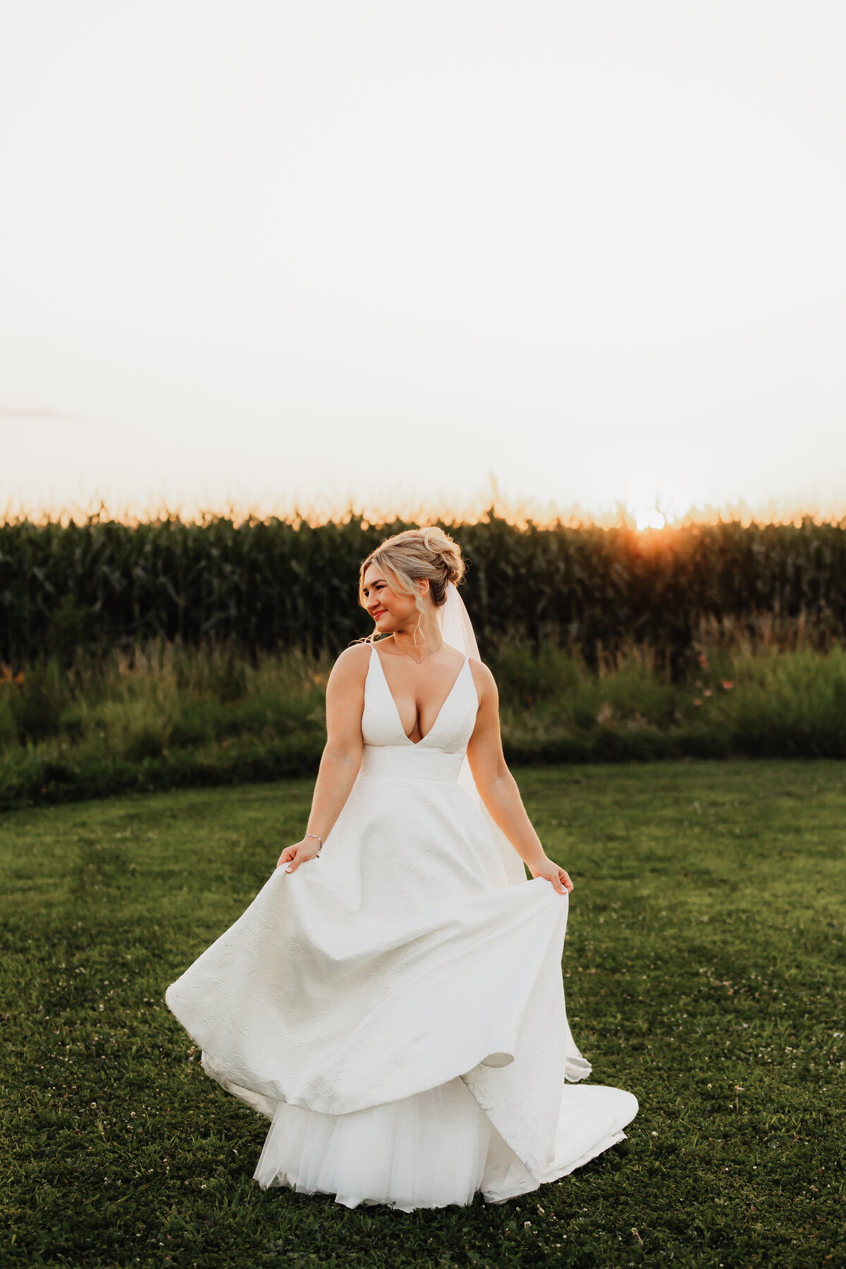 A bride looks out into a field while dancing in front of a corn field.