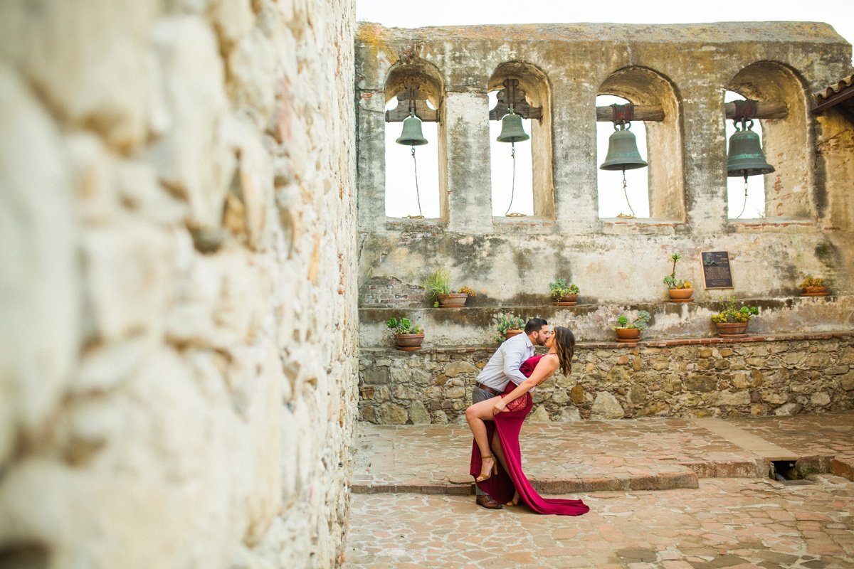Groom to be dips and kisses his fiance during engagement session at the Mission San Juan Capistrano