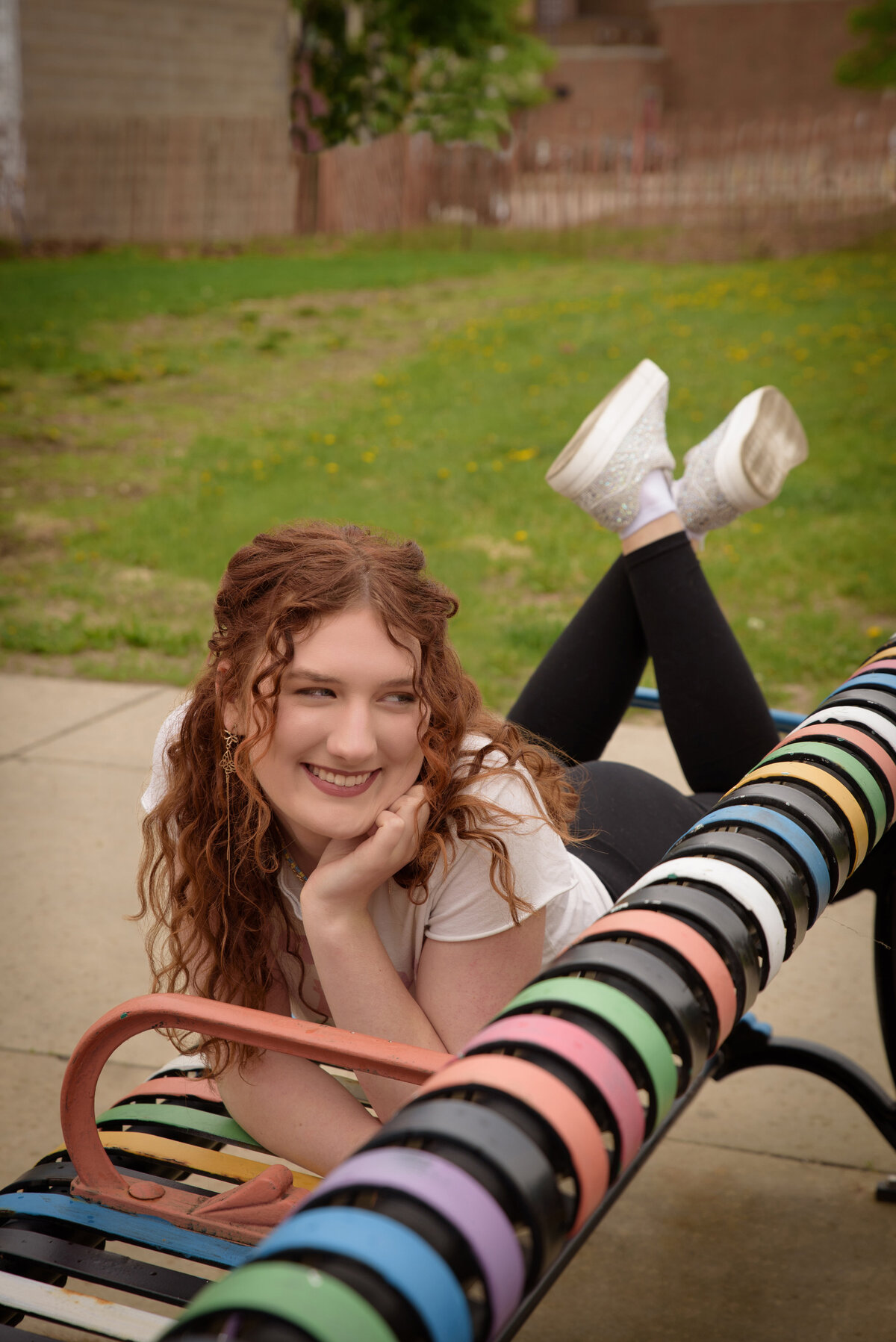 Green Bay East High School senior girl wearing a graphic t-shirt and leggings laying on her stomach on a painted metal bench in an urban setting in downtown Green Bay, Wisconsin.