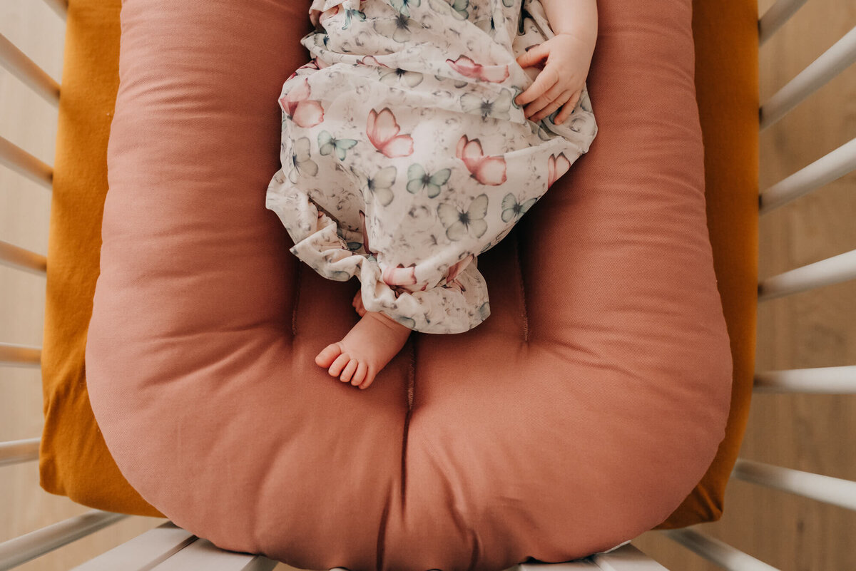 A close up image of a newborn baby's foot as she sleeps in a rose colored snuggleme