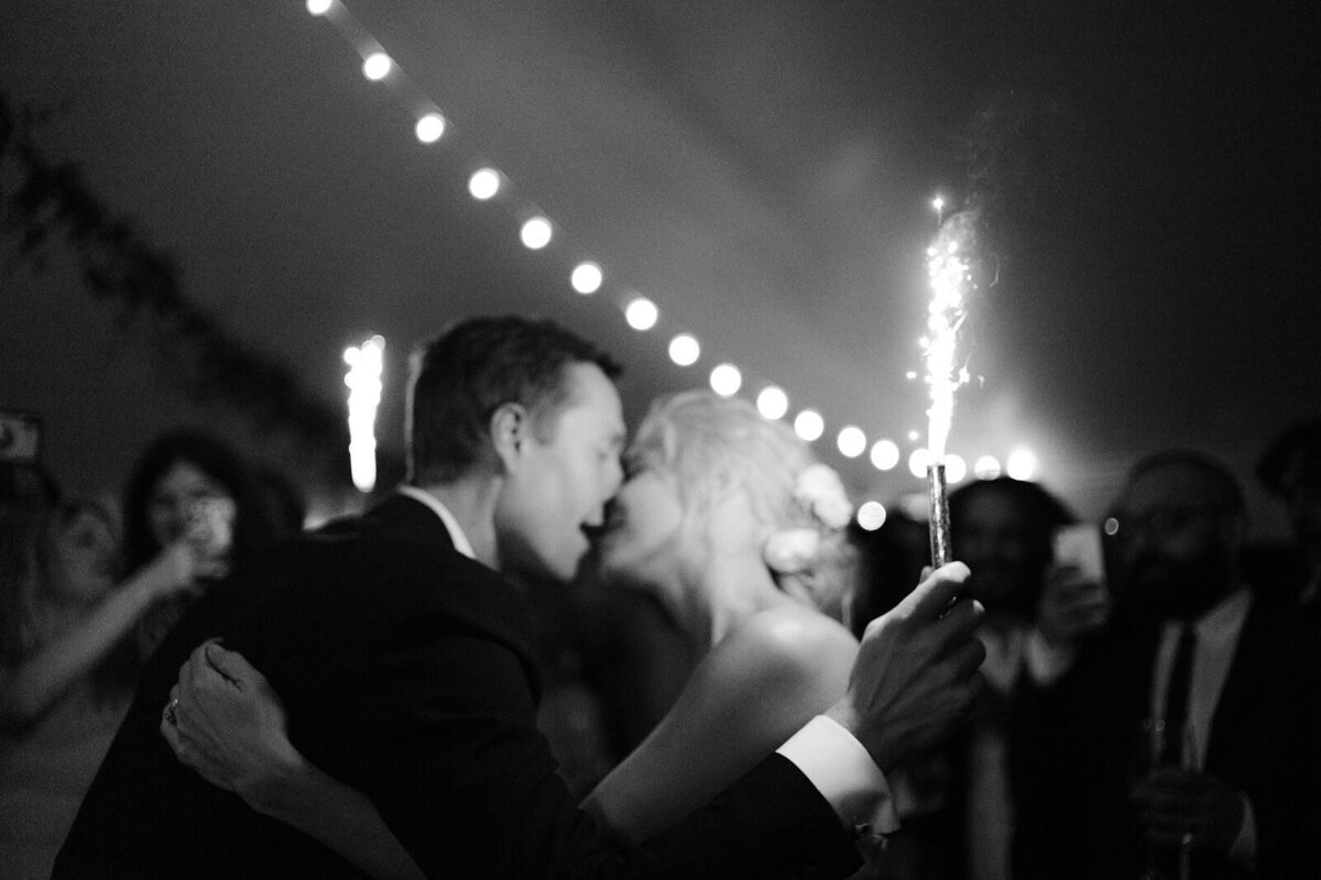 The bride and groom are kissing as they hold sparklers in Foxfire Mountain House, New York. Wedding Image by Jenny Fu Studio