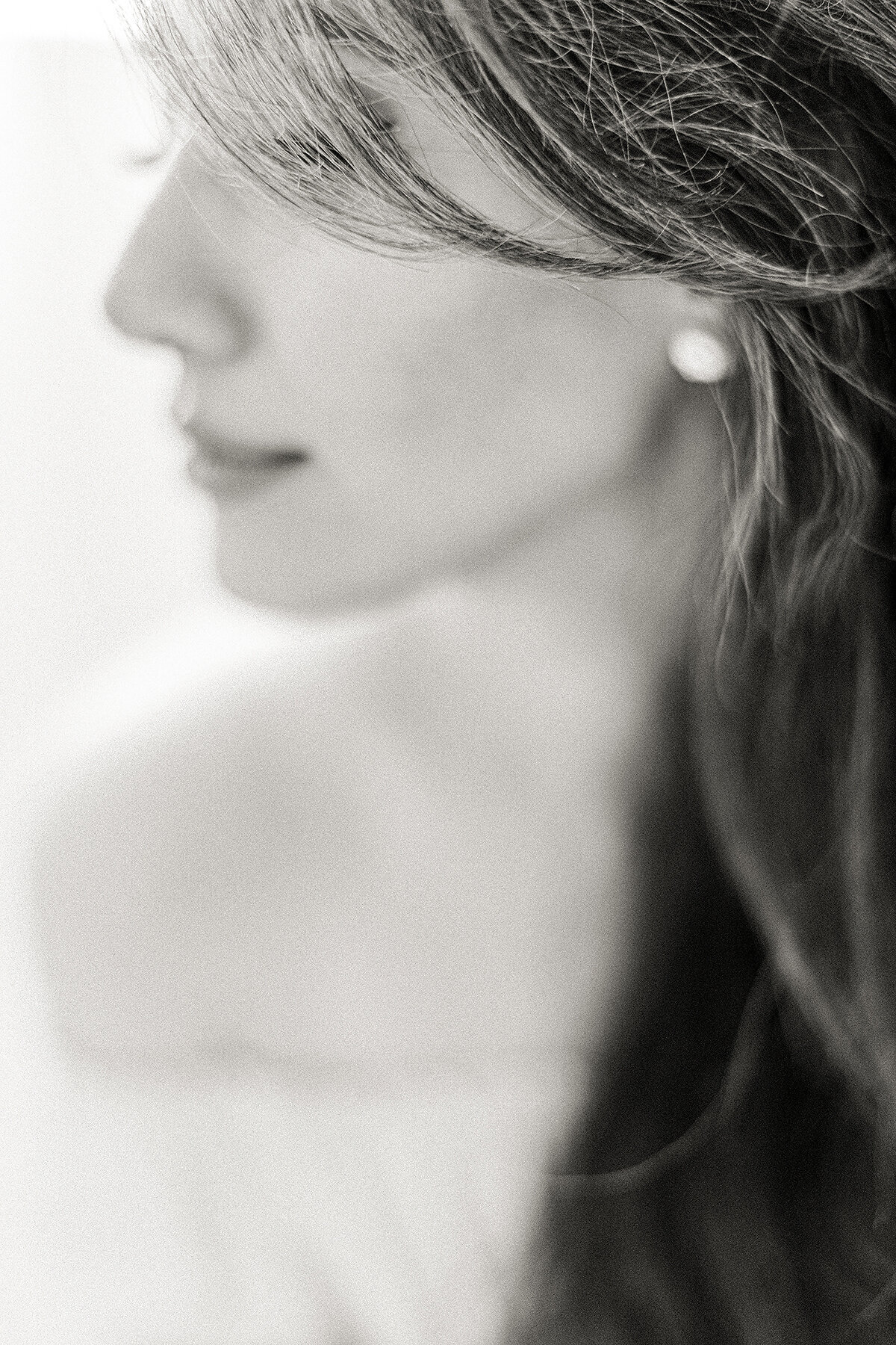 Delicate black and white close up photo of a woman with her hair gently draped of her hair as she looks down and smiles.