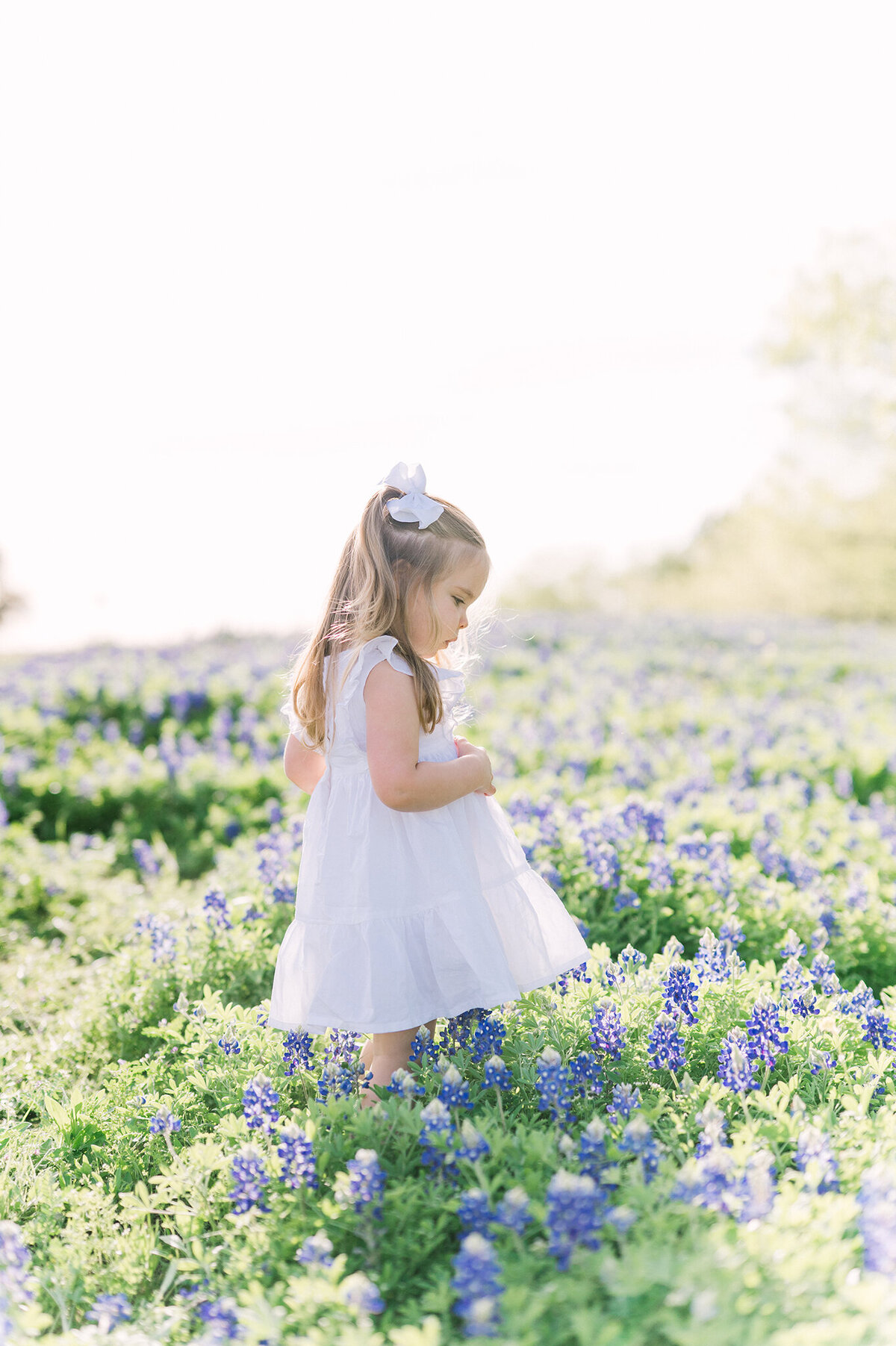 Young girl with long blonde hair frolicking through a bluebonnet field.