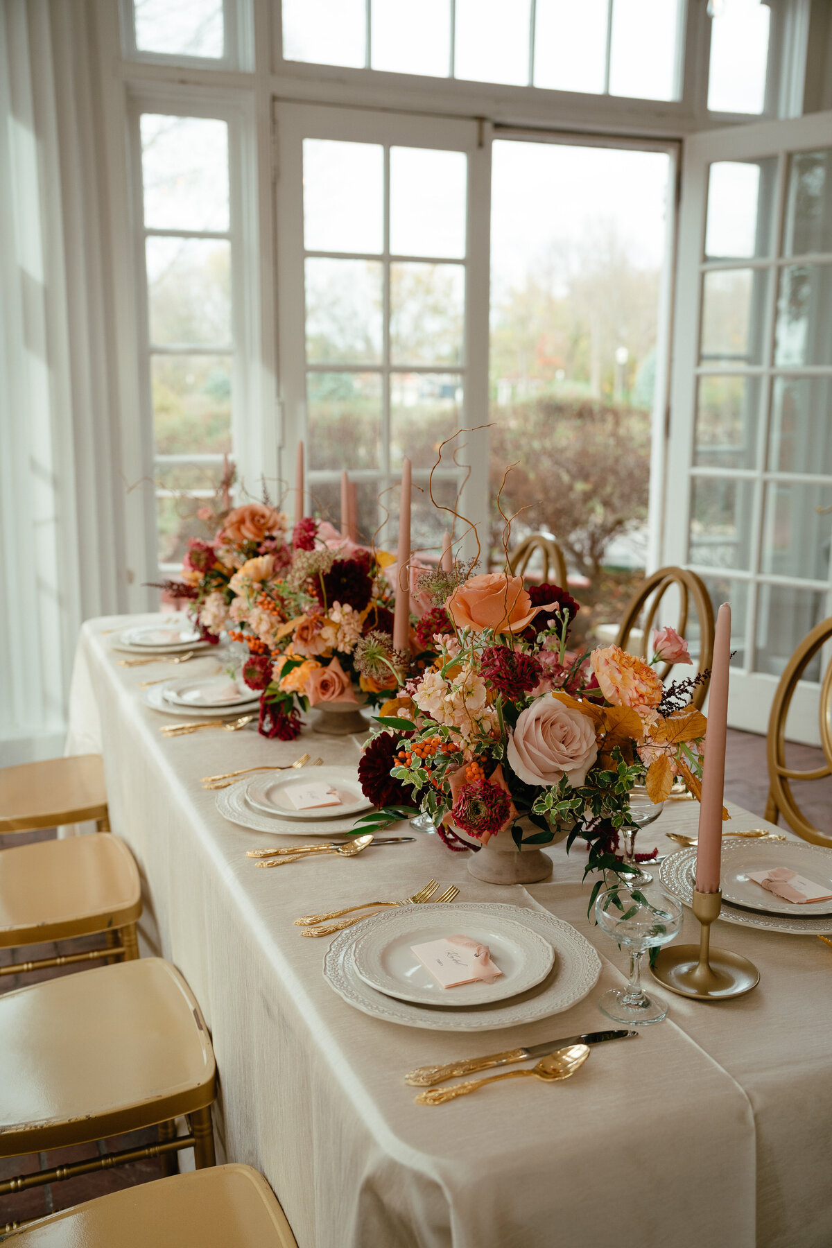 A table set with fine china and many pink and orange floral arrangements