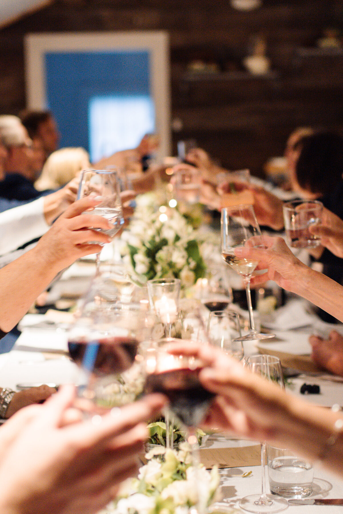 Hands reach together to toast the wedding couple with white florals by Adam