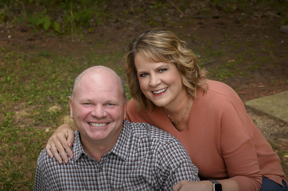 Mom hugs Dad as they sit on the grass