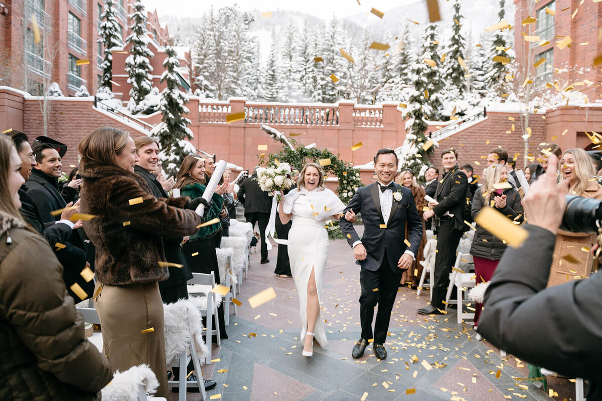 Bride and groom walking down the aisle during their ceremony recessional at St. Regis Aspen, smiling and holding hands.