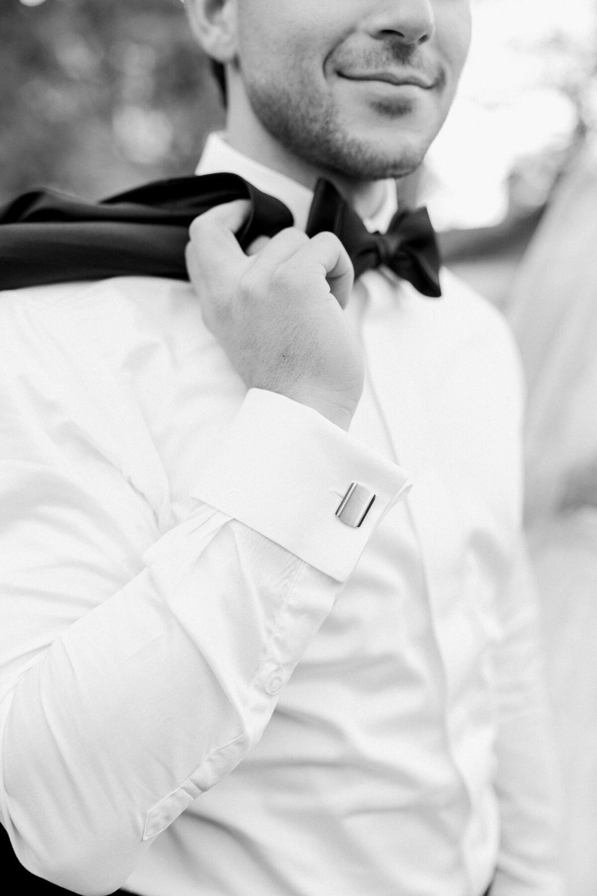 Man in a formal white shirt adjusting his black bow tie.