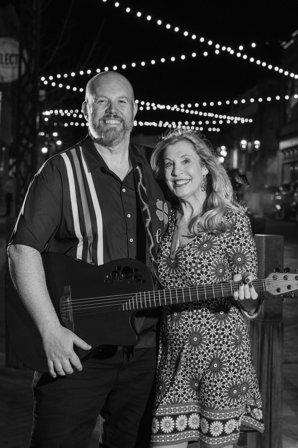 Black and white photo of two people smiling while one holds a guitar 