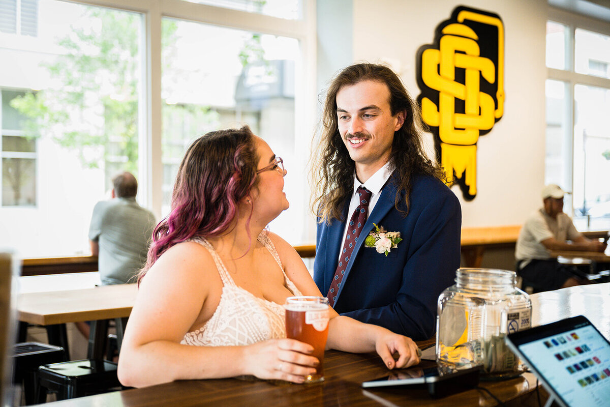 A couple on their elopement day wait at the bar of Olde Salem Brewery in Downtown Roanoke to pay for their beers and look and smile at one another.