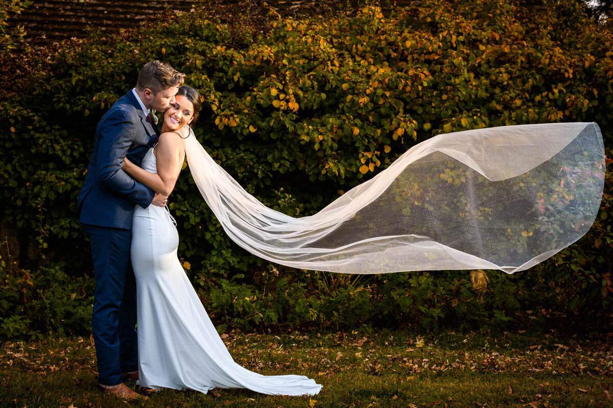 A bride's long veil trails beautifully behind her in the breeze as her groom embraces her