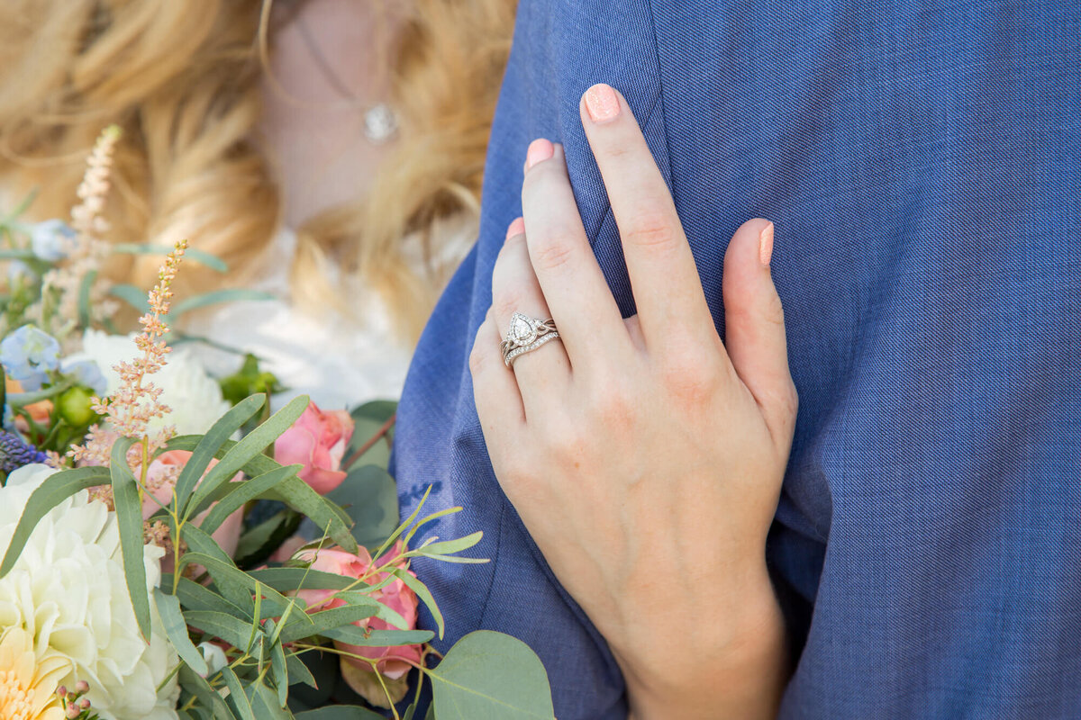 a bride's hand with a wedding band holding grooms arm