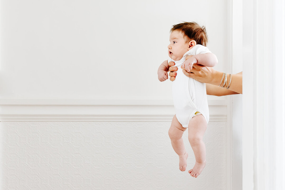 Baby girl with a dirty diaper is held at a distance. 