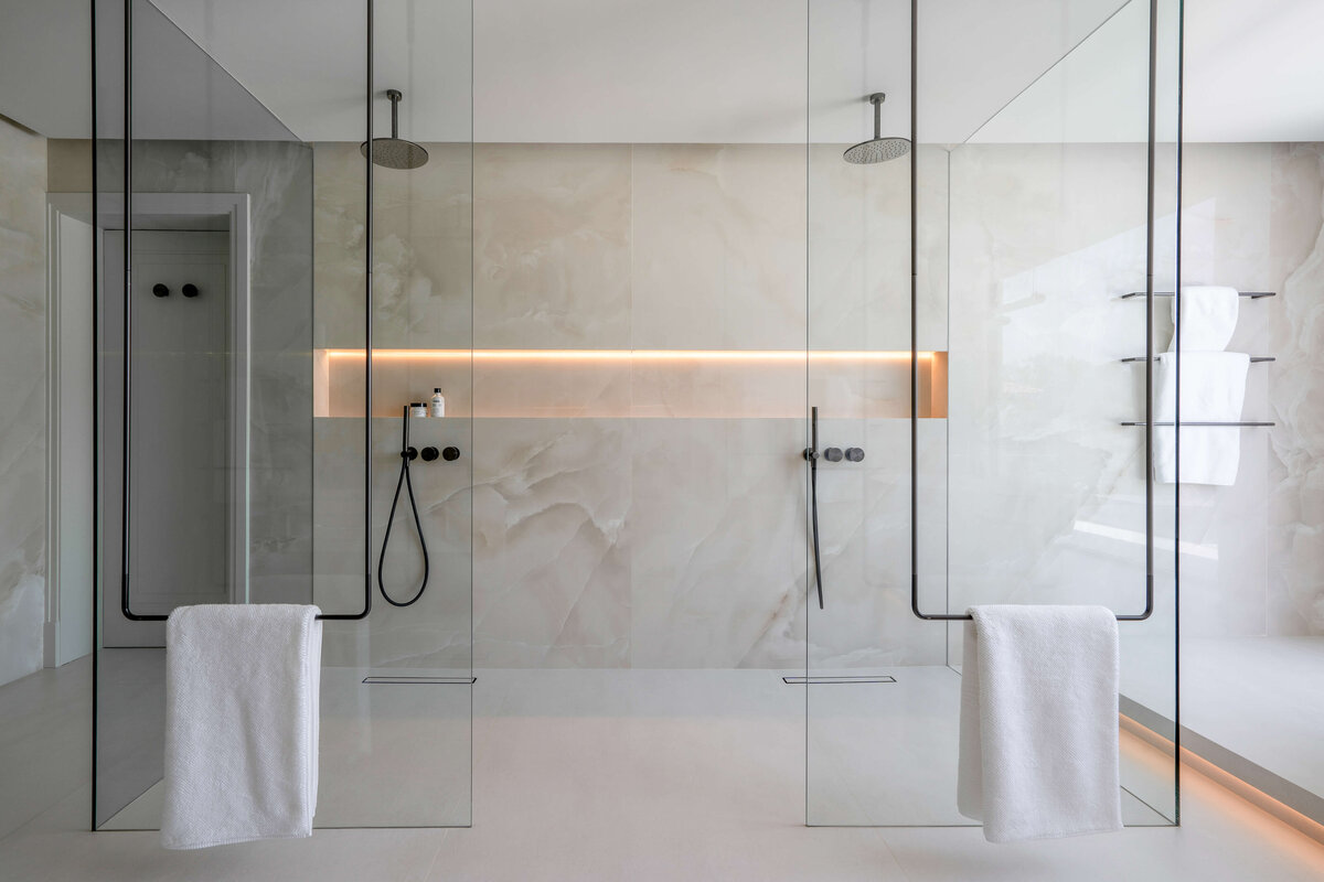 A large walk-in glass double shower with neutral marble walls and black hardware.