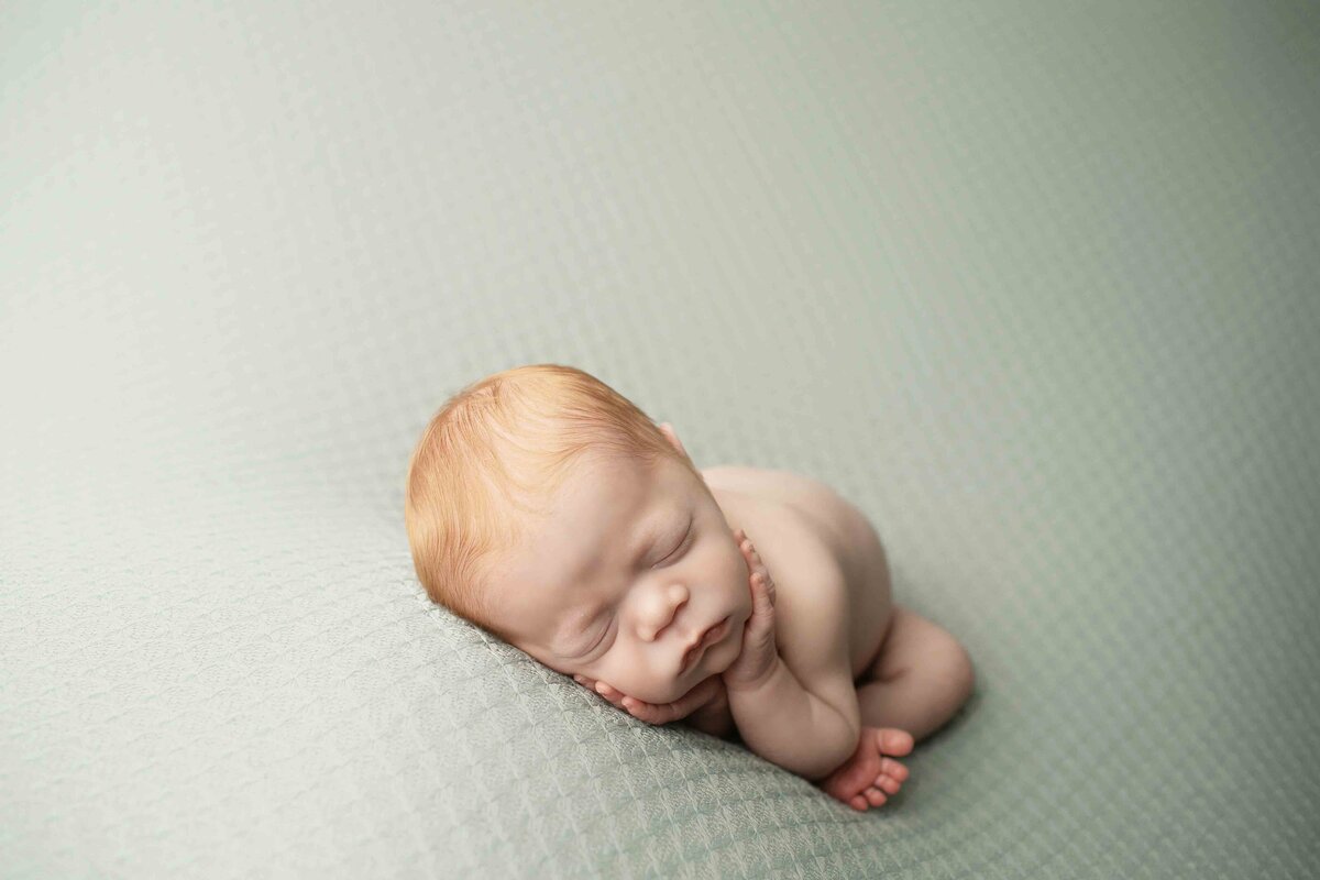 Tiny redhead newborn baby boy resting peacefully on a soft, knitted blanket