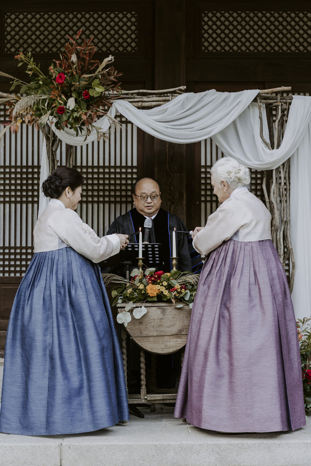 mothers dressing in blue and purple hanbok lighting a candle at wedding