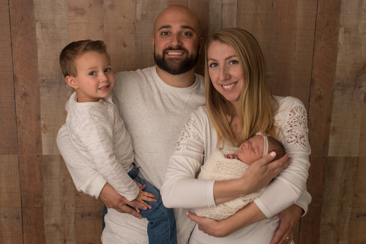 Family in neutral colors, holding baby girl wrapped in white swaddle