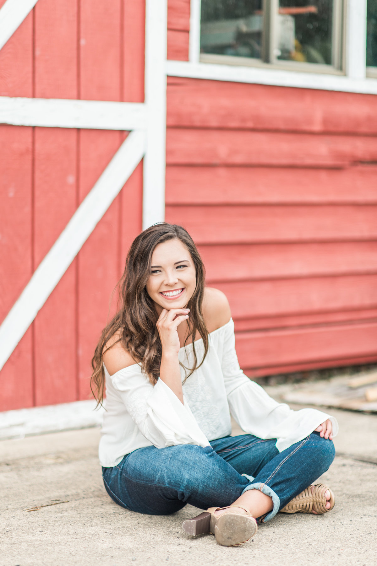 Cute teen sitting cross legged in front of a red barn door.