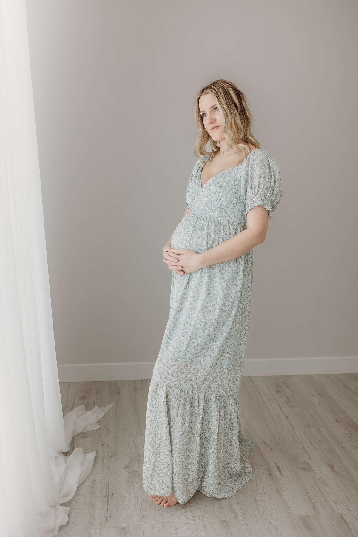 Full length portrait by window of expecting mom in dress for maternity pictures