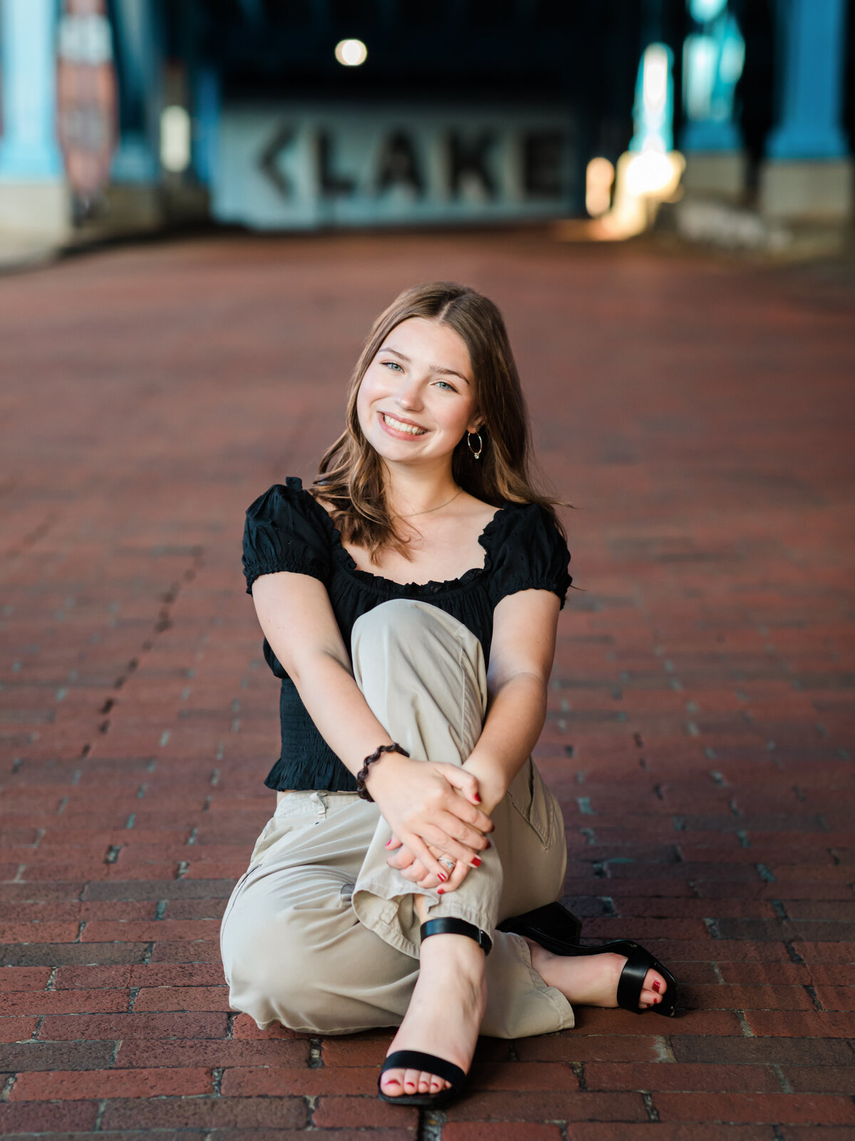 senior girl in black shirt sitting brick road for senior photos