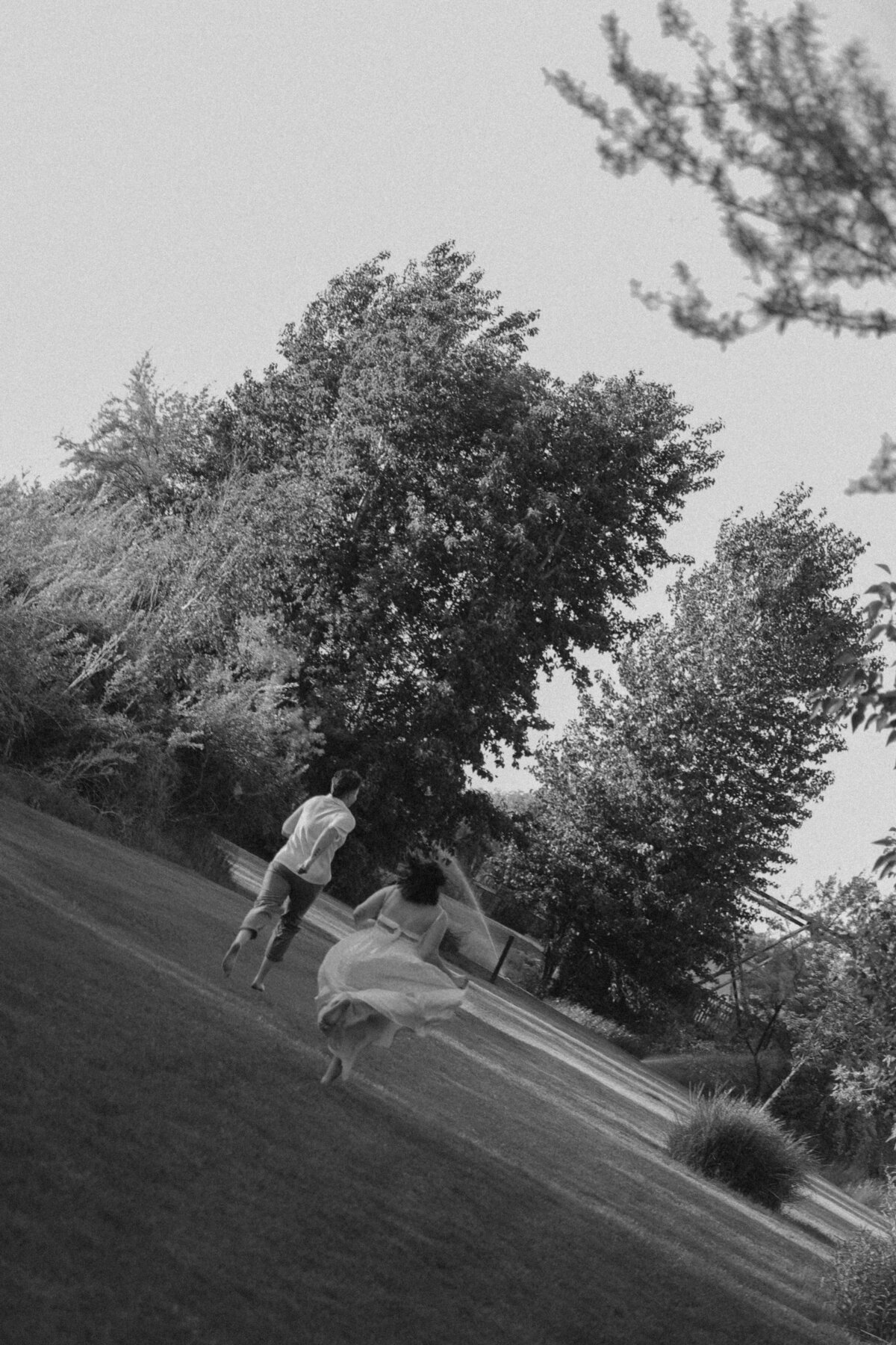Candid Wedding Moment of Couple Running Hand in Hand Through Open Field