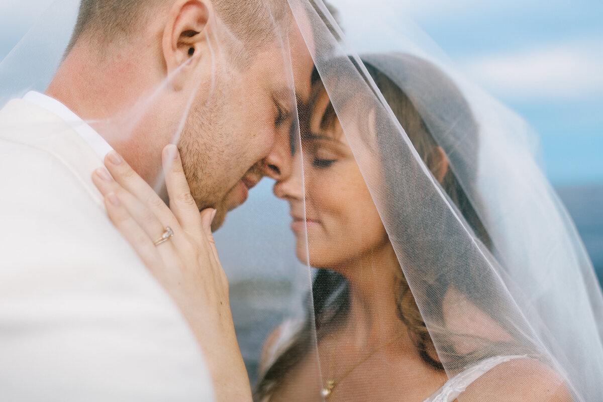 bride and groom touching their foreheads under her veil on the rock at North shore