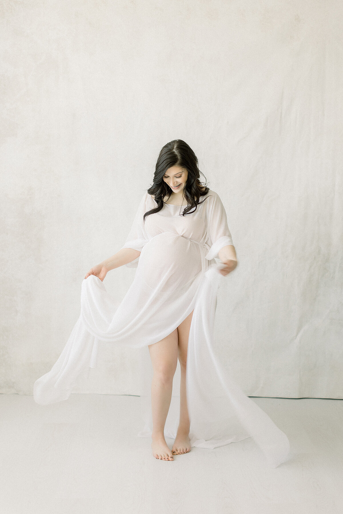 A photo taken for a maternity session in a Dallas/Fort Worth area photography studio of an expecting mother while she is playfully swaying around her chiffon maternity dress.