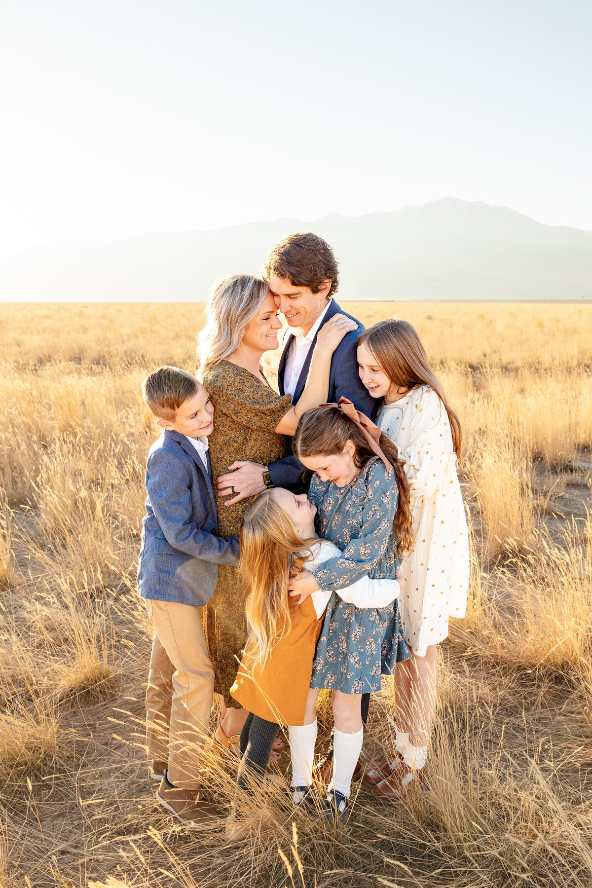 A heartwarming moment of a mother and father embracing their children closely in a sunlit field 