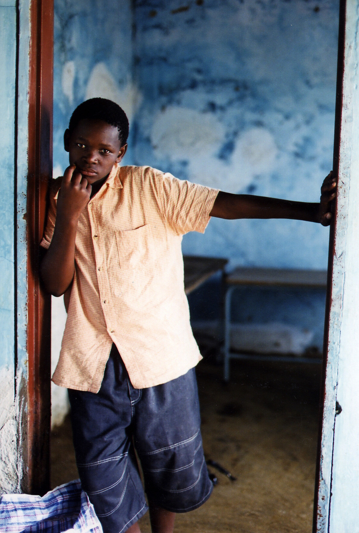 A portrait of a South African boy leaning in a  doorway with blank stare - Editorial photo