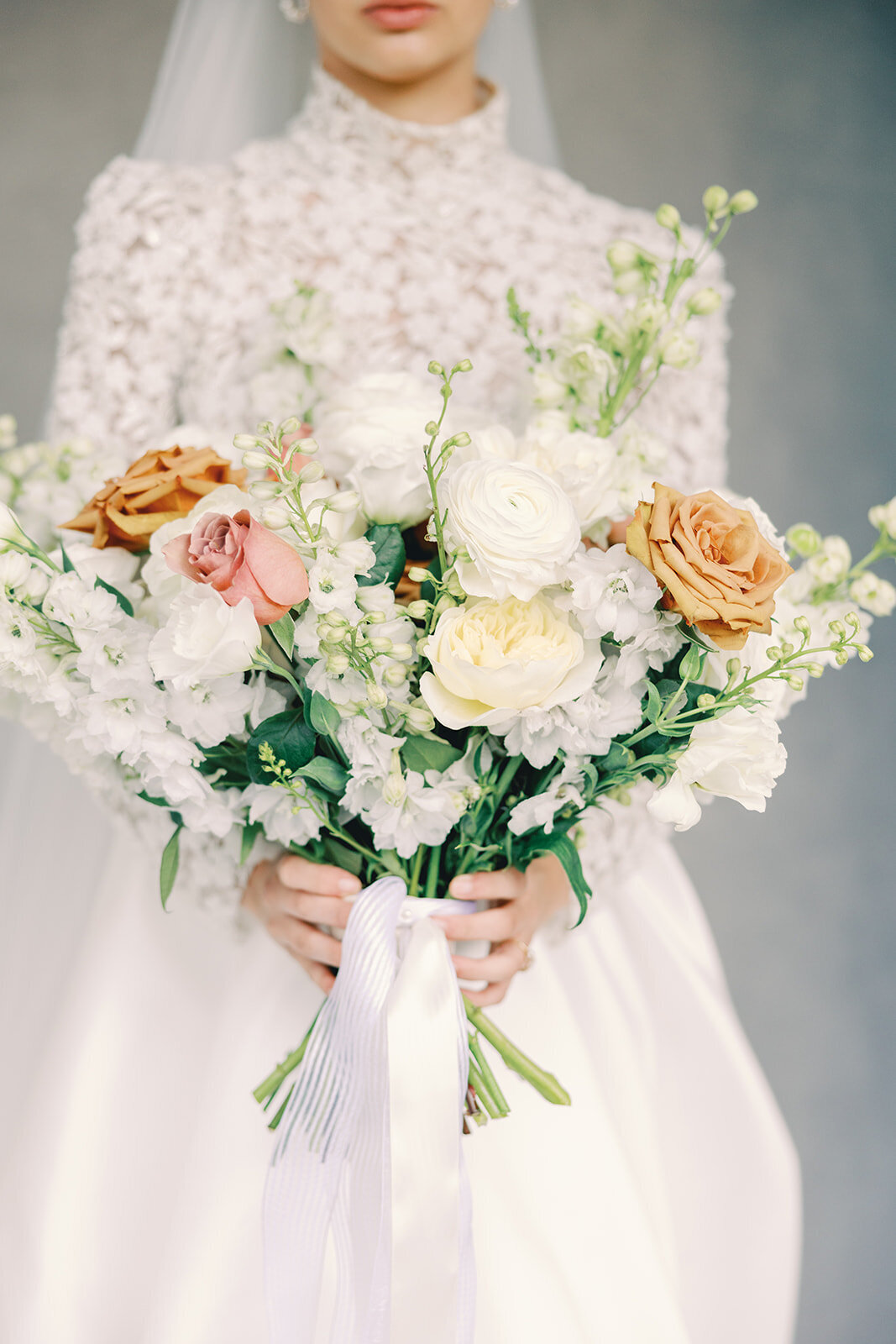 Close-up of a bride holding a large white, pink, orange and green bouquet
