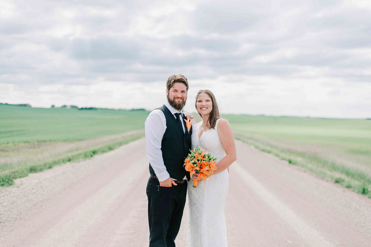 Bride and groom standing together on a gravel road.