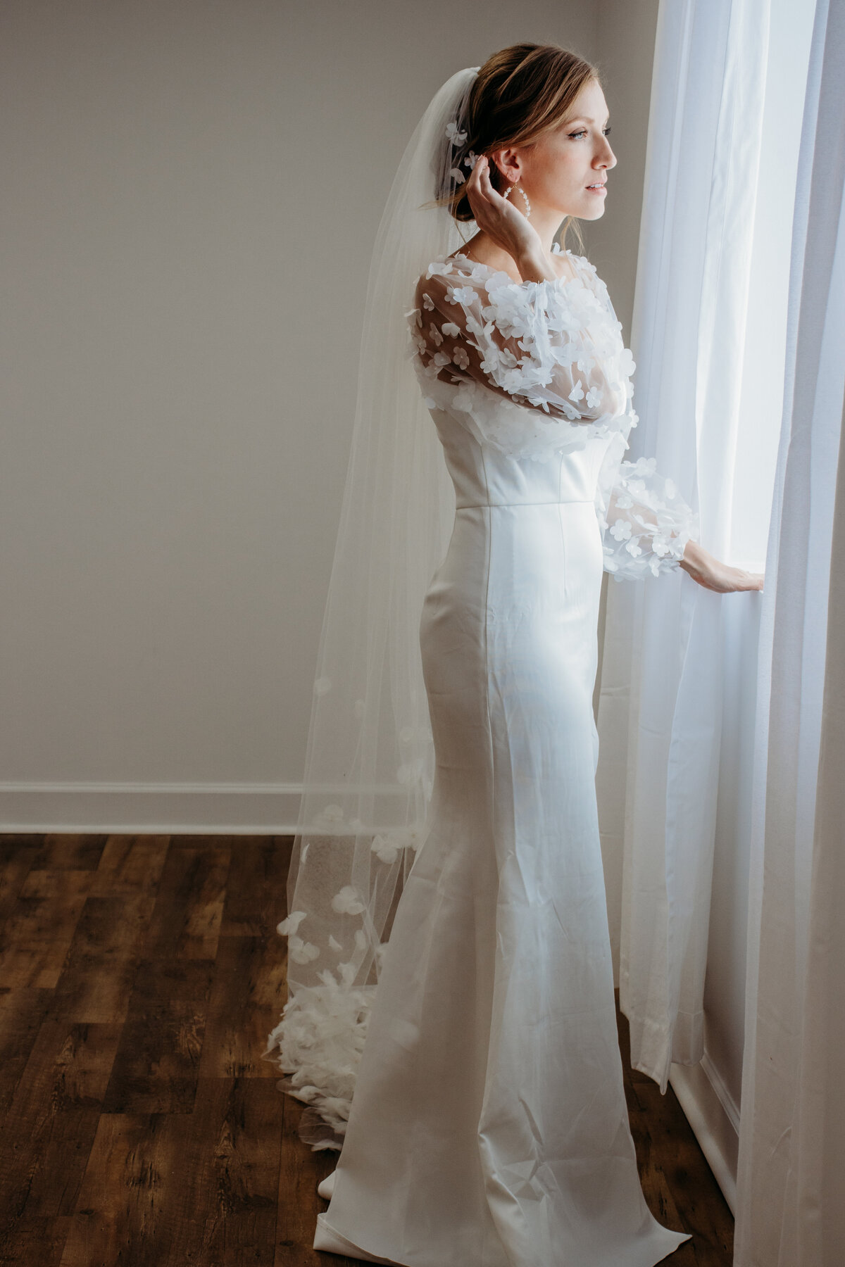 A bride poses in the window as natural light shines in before her Duluth wedding ceremony.