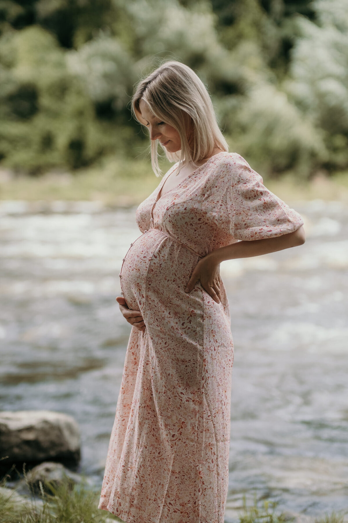 Outdoor picture of a pregnant woman with a lake in the background.